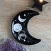 Black ceramic trinket dish with in crescent moon shape with moon and stars design, shown with rings in it as an example