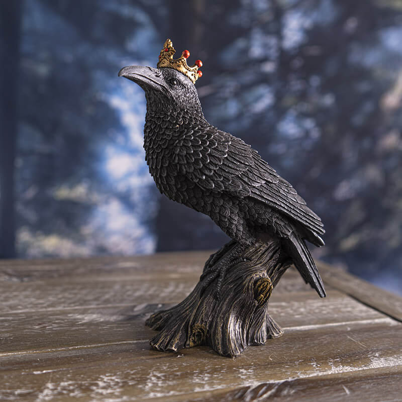 Figurine of a black crow on a branch wearing a golden crown with red accents