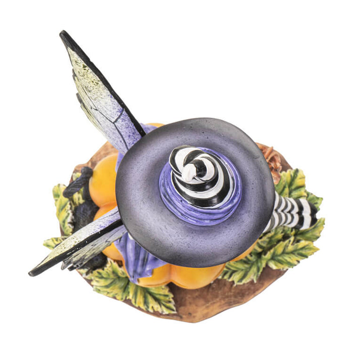 Figurine of a fairy in black and white stripes with purple and green accents sitting on a pumpkin next to a black cat. Top down view