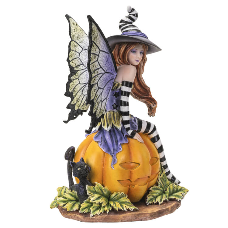 Figurine of a fairy in black and white stripes with purple and green accents sitting on a pumpkin next to a black cat