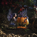 Dark haired fairy with purple wings and dress and striped sleeves & Stockings kneels in front of a pumpkin with a periwinkle dragon popping out, shown in a display setting