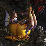 Fairy with red hair, black cat, and orange-purple dragon sitting in a bright orange pumpkin amidst fall leaves, shown in display setting