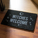 Black doormat with text of "WITCHES WELCOME" in white with stars and a moon
