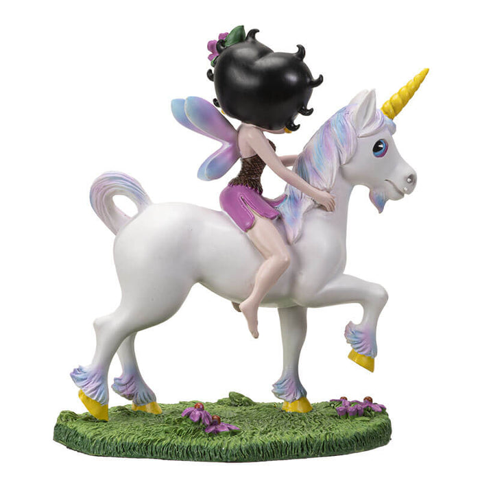 Figurine of Betty Boop with fairy wings and purple flowers in her hair, riding a unicorn in a grassy meadow shown from the back