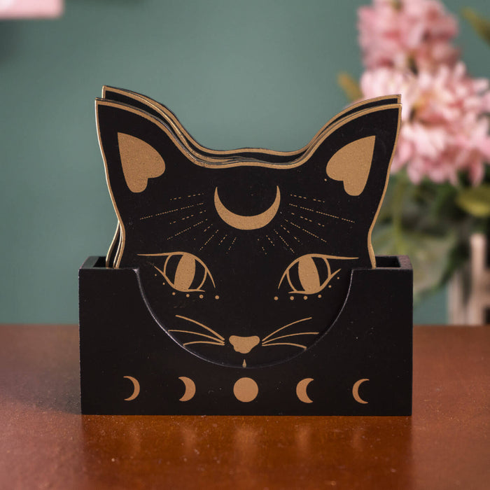 Set of coasters featuring black cat heads with gold accents and moon motif, with matching holder