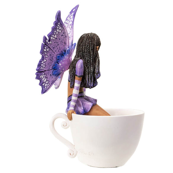 Figurine of a fairy with purple wings and dress and dark skin sitting on the edge of a teacup
