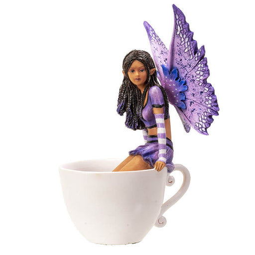 Figurine of a fairy with purple wings and dress and dark skin sitting on the edge of a teacup