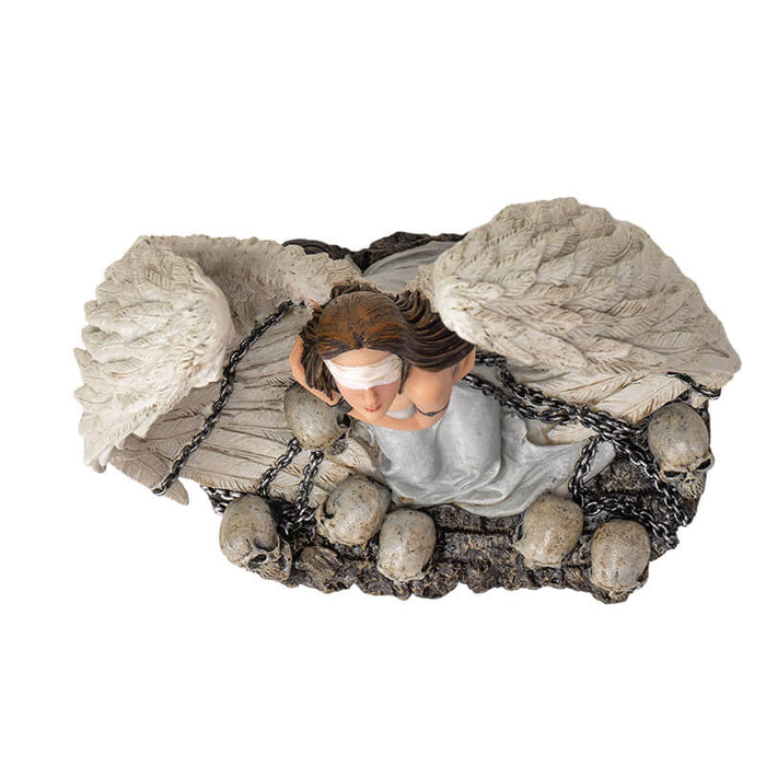 Figurine of a white winged angel woman in chains, blindfolded sitting amongst skulls. Top down view