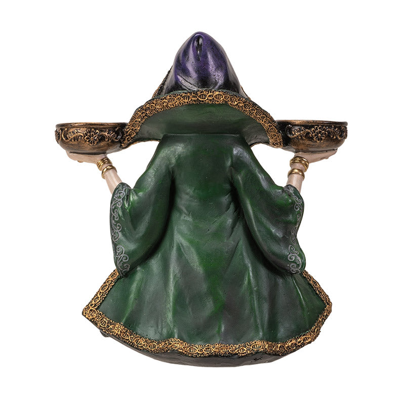 Decorative figurine of a witchy woman in a green cloak and purple dress holding two bowls into which candles can sit, shown from the back