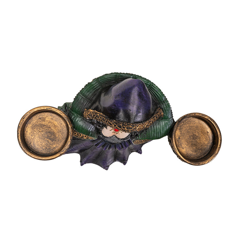 Decorative figurine of a witchy woman in a green cloak and purple dress holding two bowls into which candles can sit, shown top down