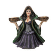 Decorative figurine of a witchy woman in a green cloak and purple dress holding two bowls into which candles can sit
