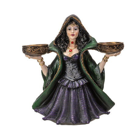 Decorative figurine of a witchy woman in a green cloak and purple dress holding two bowls into which candles can sit