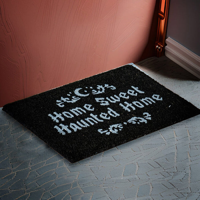 Black doormat with the phrase "Home Sweet Haunted Home" in white, with swirl and moon design above and below