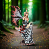 Figurine of a fairy in pale blue dress holding quill and parchment with a small red dragon