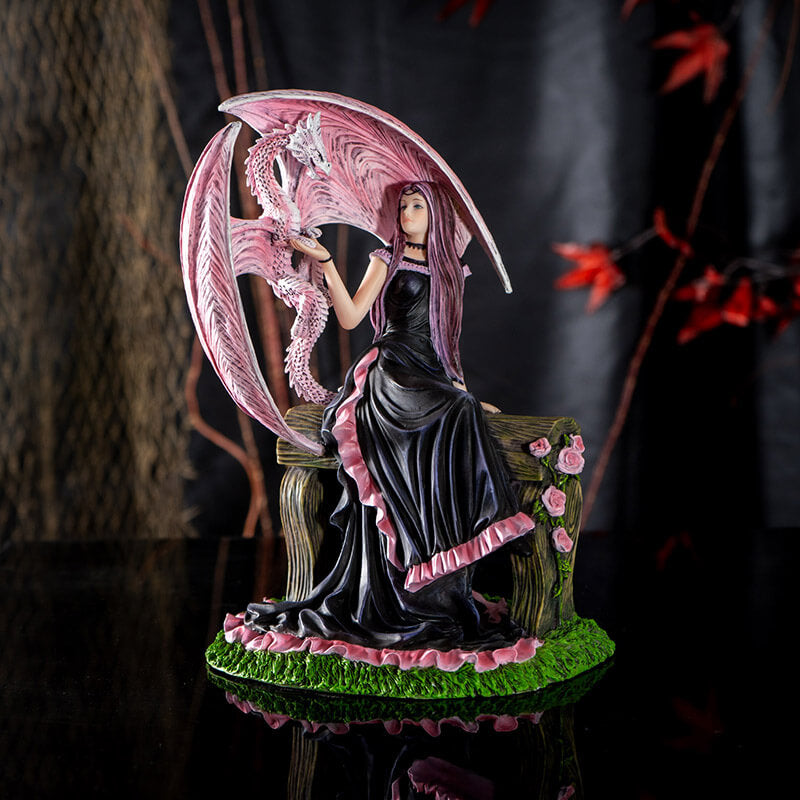 Figurine based on the artwork of Anne Stokes - woman in black and pink dress sitting on a bench with roses, holding the claw of a pink dragon