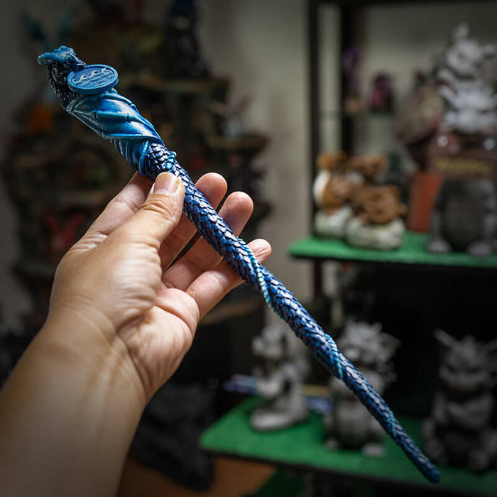 Blue magic wand with a dragon and wave emblem and scales down the length, held in a hand