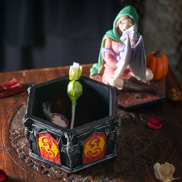 Trinket box, lid has a woman in a green cloak and pink dress cuddling a purple dragon, with a pumpkin. Outer rim of box has red and yellow dragon designs. Shown with some candy inside, lid off