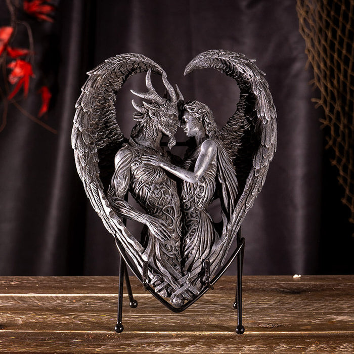 Figurine on stand of demon and angel forming a heart with their wings, done in faux-stone.