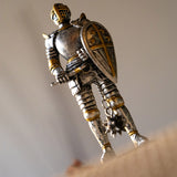 Figurine of a knight in silver armor with gold accents holding a shield and a flail