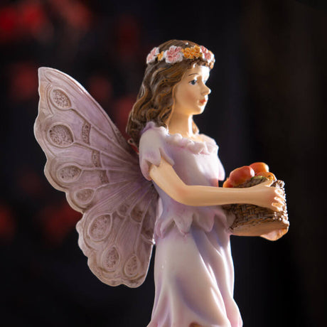 Figurine of a fairy with brown hair and flower crown carrying a basket of apples.