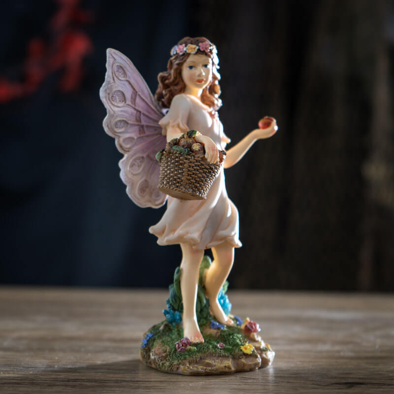 Fairy figurine of pixie with basket full of fruit, holding one. Brown hair, flower corn, pale pink dress & wings