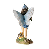 Figurine of fairy in a blue dress with flower hat and pale wings holding bouquet of pink flowers with more blooms at her feet. Back view