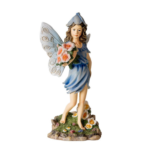 Figurine of fairy in a blue dress with flower hat and pale wings holding bouquet of pink flowers with more blooms at her feet.
