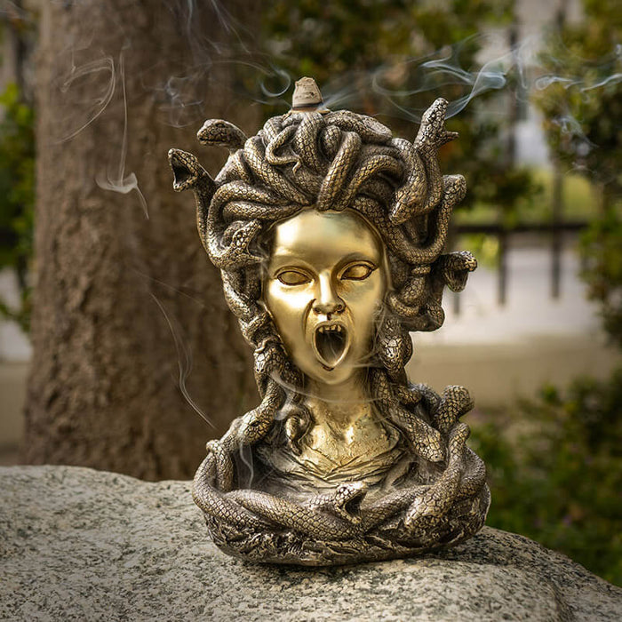 Backflow incense burner shaped like medusa's face with open mouth for smoke, snake hair. Done in faux-bronze.
