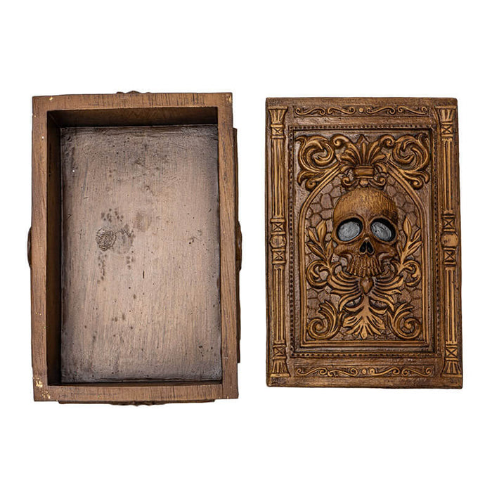 Tarot or trinket box in brown hue with skull and elaborate designs on lid, more fleur de lis emblems on the side. Shown open, top down