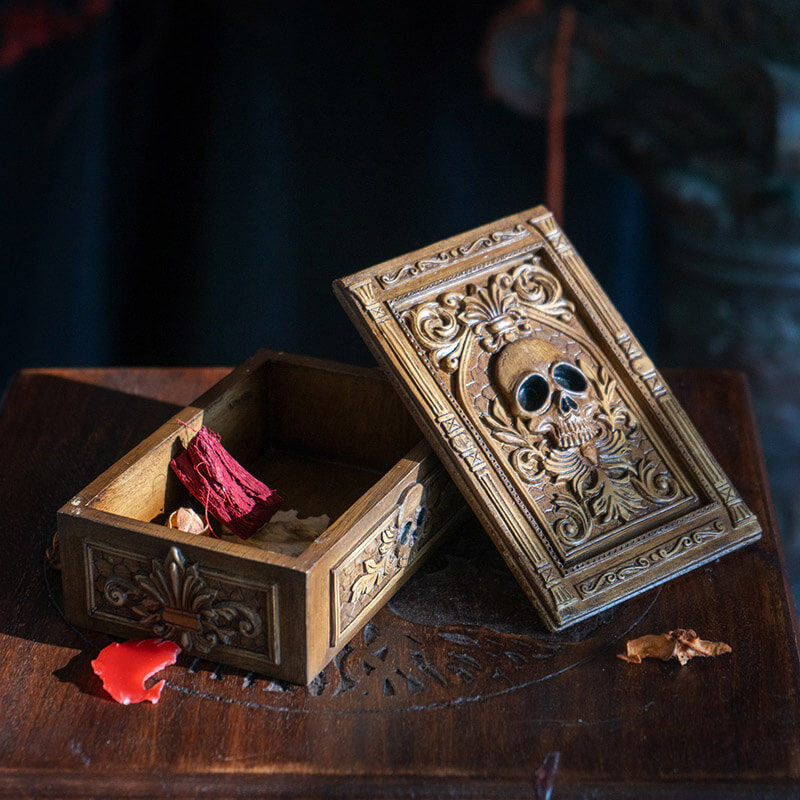 Tarot or trinket box in brown hue with skull and elaborate designs on lid, more fleur de lis emblems on the side.