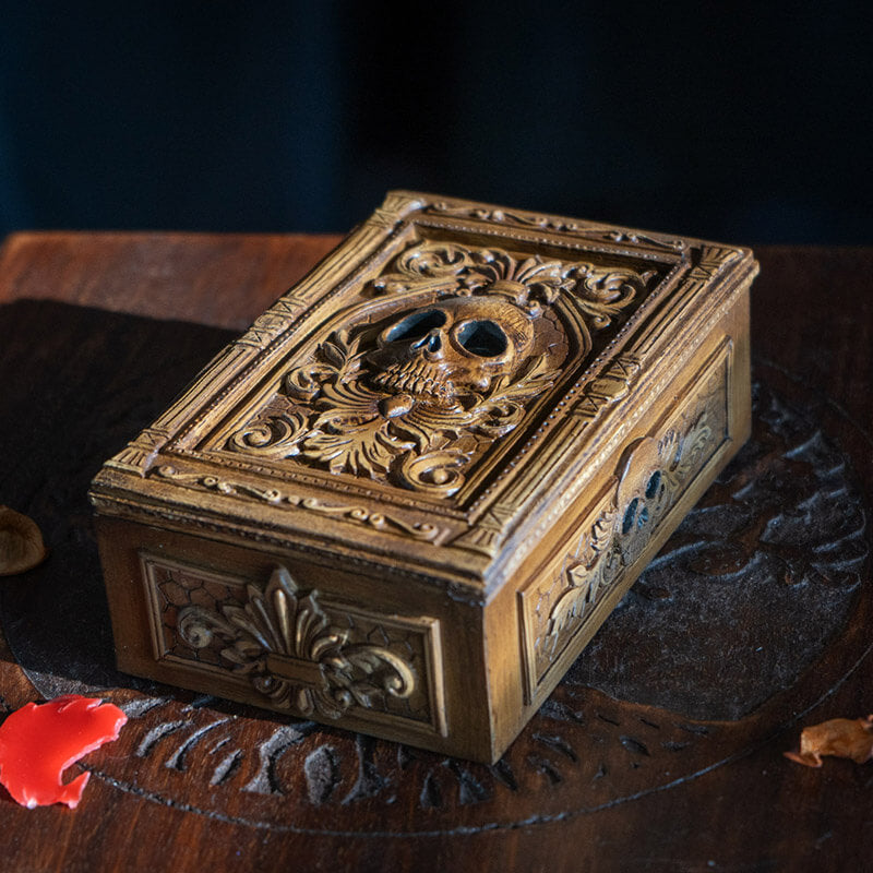 Tarot or trinket box in brown hue with skull and elaborate designs on lid, more fleur de lis emblems on the side.