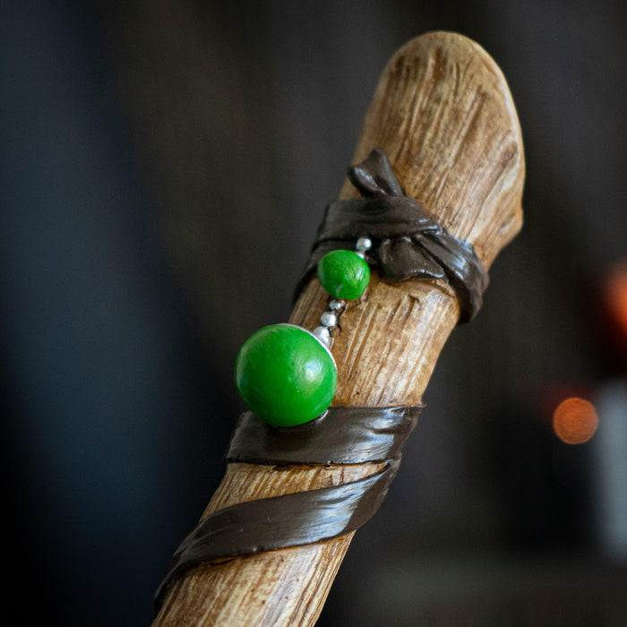 Magic wand in faux wood banded with  ribbon accents, baubles and carved with runes.
