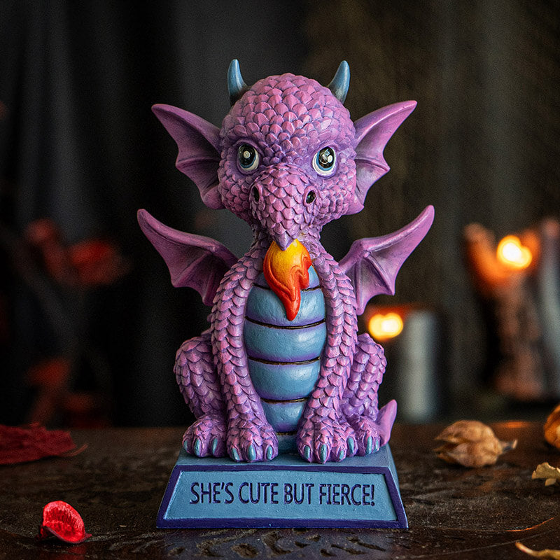 Figurine of a pink dragon with blue tummy and horns and a flame, sitting on indigo base that reads "She's cute but fierce!"