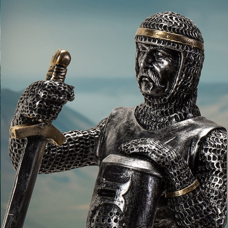 faux-metallic figurine of a medieval knight kneeling, holding helm and sword, wearing chainmail with gold accents