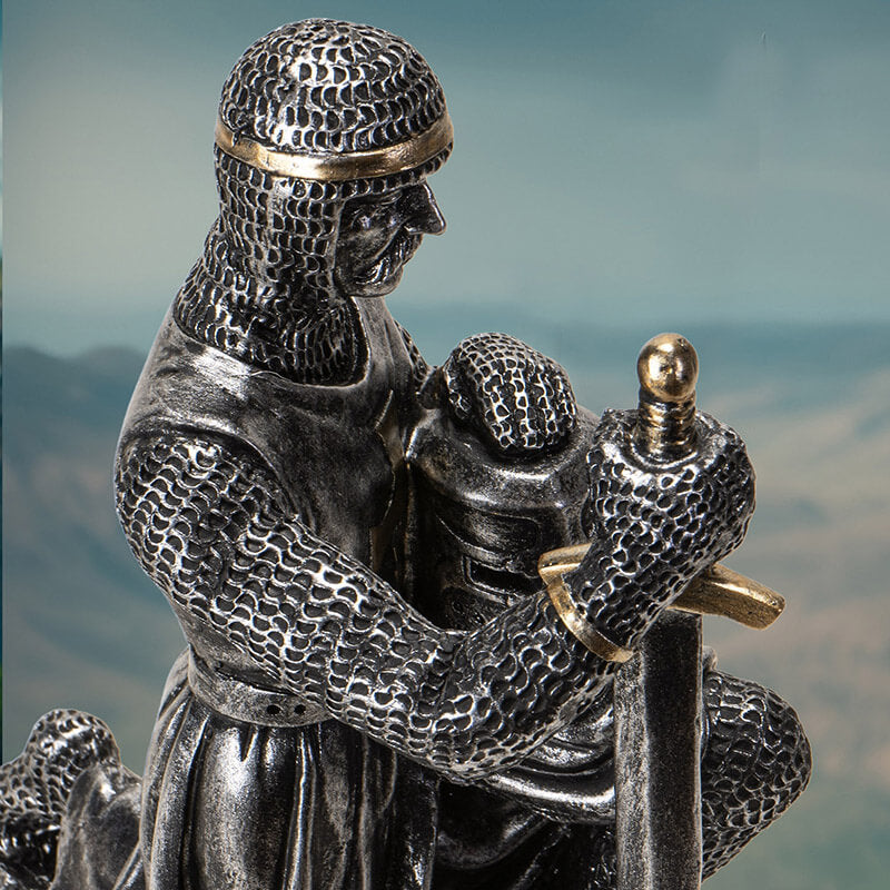 faux-metallic figurine of a medieval knight kneeling, holding helm and sword, wearing chainmail with gold accents