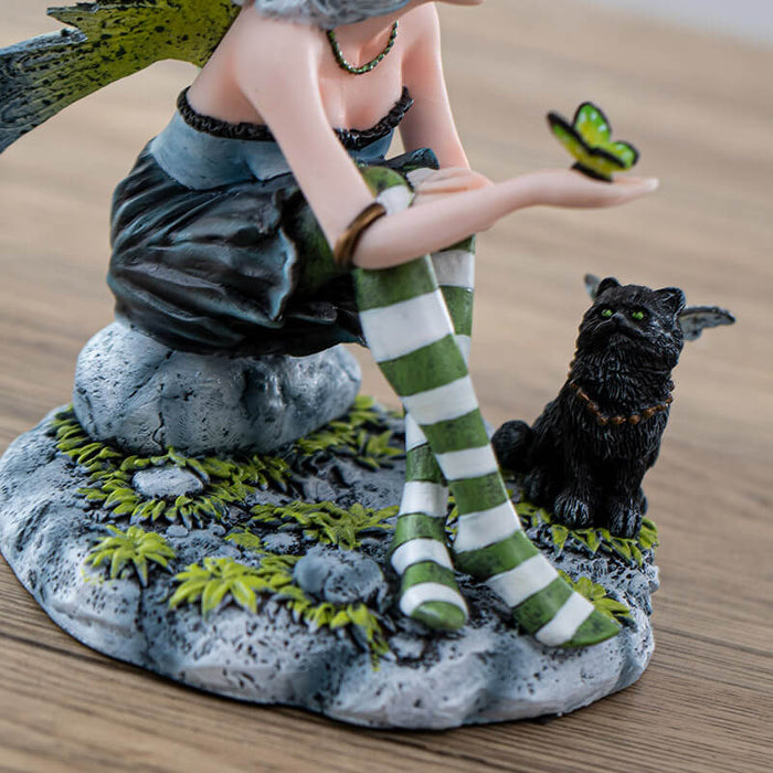 Figurine of fairy with green wings and striped stockings, and black cat ears. Holding a butterfly with a black winged fairy cat next to her. 