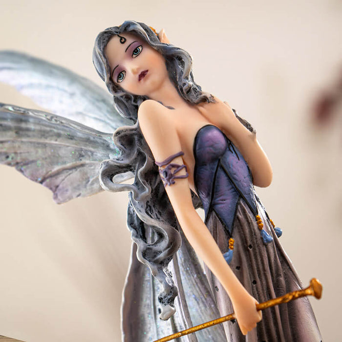 Figurine of fairy with gray wings and hair and purple dress walking with two tan wolves. Fae carries a gold wand.