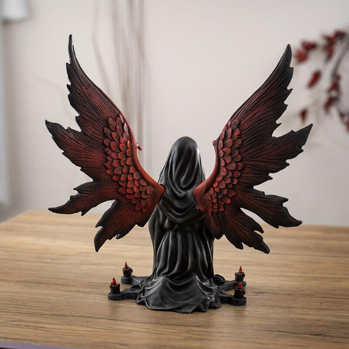 Figurine of an angel with red wings and hair in a black cloak, holding a crystal ball sitting at the center of a star with purple roses and candles, shown from the back