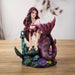 Figurine of mermaid with pink hair and magenta and black striped tail sitting with an anchor, fish, skull and coral