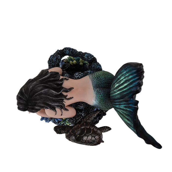 Figurine of black haired mermaid with green and blue tail resting on coral reef with a dark sea turtle
