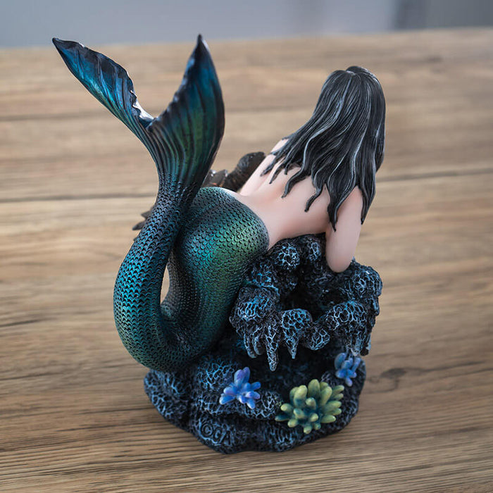 Figurine of black haired mermaid with green and blue tail resting on coral reef with a dark sea turtle