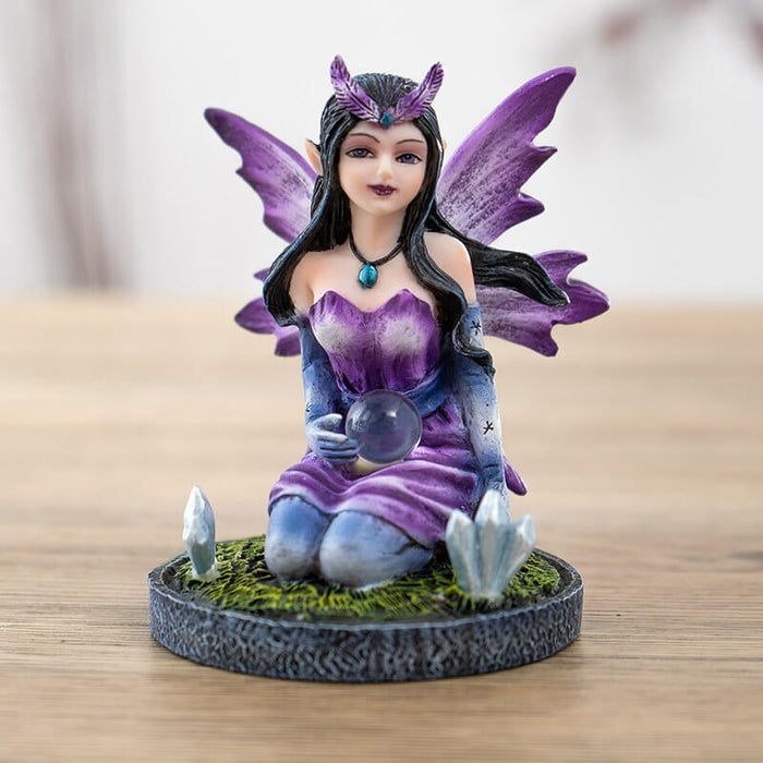 Figurine of a purple winged and dress fairy kneeling with a crystal ball and gems growing next to her