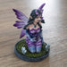 Figurine of a purple winged and dress fairy kneeling with a crystal ball and gems growing next to her