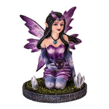 Figurine of a purple winged and dress fairy kneeling with a crystal ball and gems growing next to her