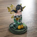 Figurine of kneeling fairy in green, black and yellow with black hair holding a crystal ball on her lap, with crystals next to her