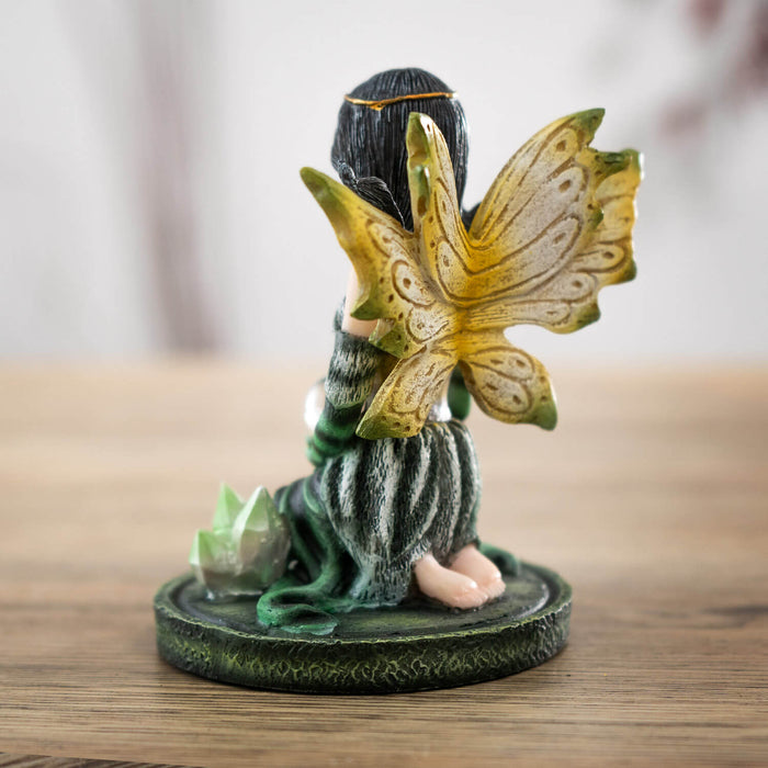 Figurine of kneeling fairy in green, black and yellow with black hair holding a crystal ball on her lap, with crystals next to her