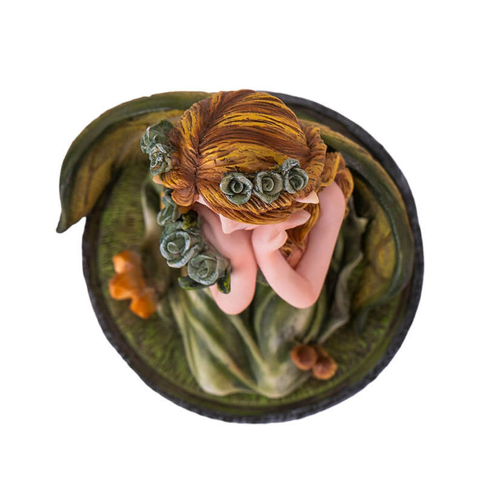 Figurine of small fairy with crystals and mushrooms where she kneels in the moss, holding a bouquet of flowers with more in her blond hair. Top down view