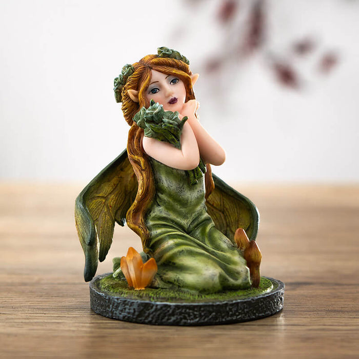 Figurine of small fairy with crystals and mushrooms where she kneels in the moss, holding a bouquet of flowers with more in her blond hair.