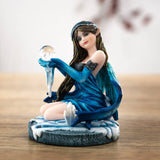 Figurine of brunette fairy in blue dress sitting in snow by a crystal cluster, holding crystal ball