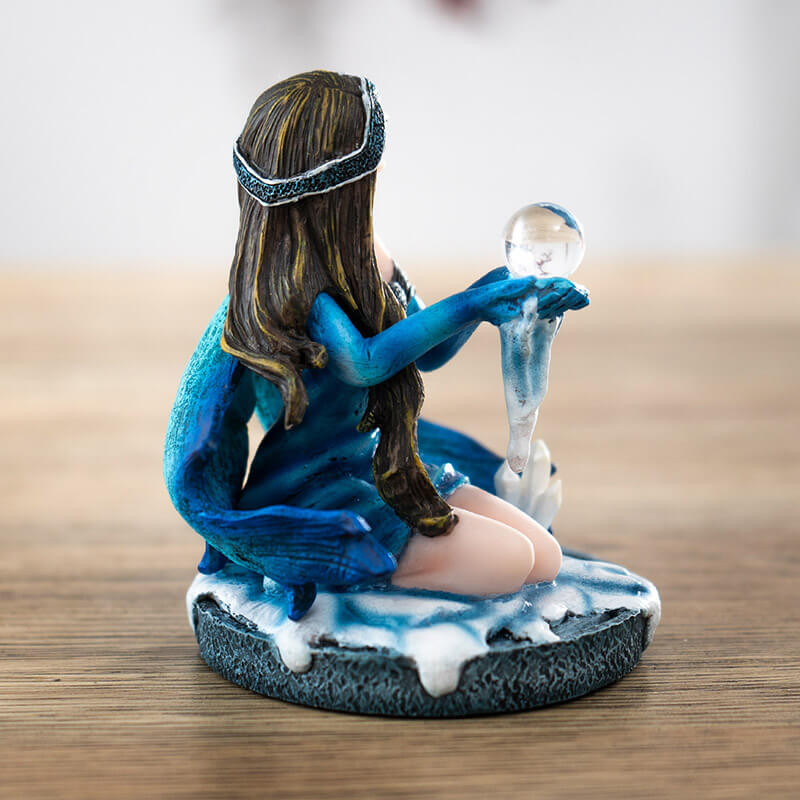 Figurine of brunette fairy in blue dress sitting in snow by a crystal cluster, holding crystal ball